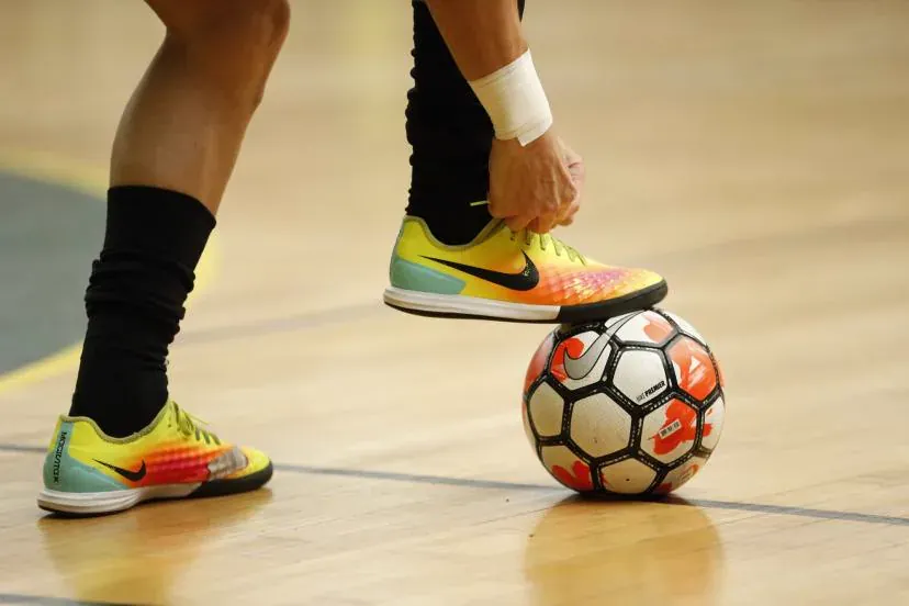 A player's foot rolling a futsal ball on a hardwood court